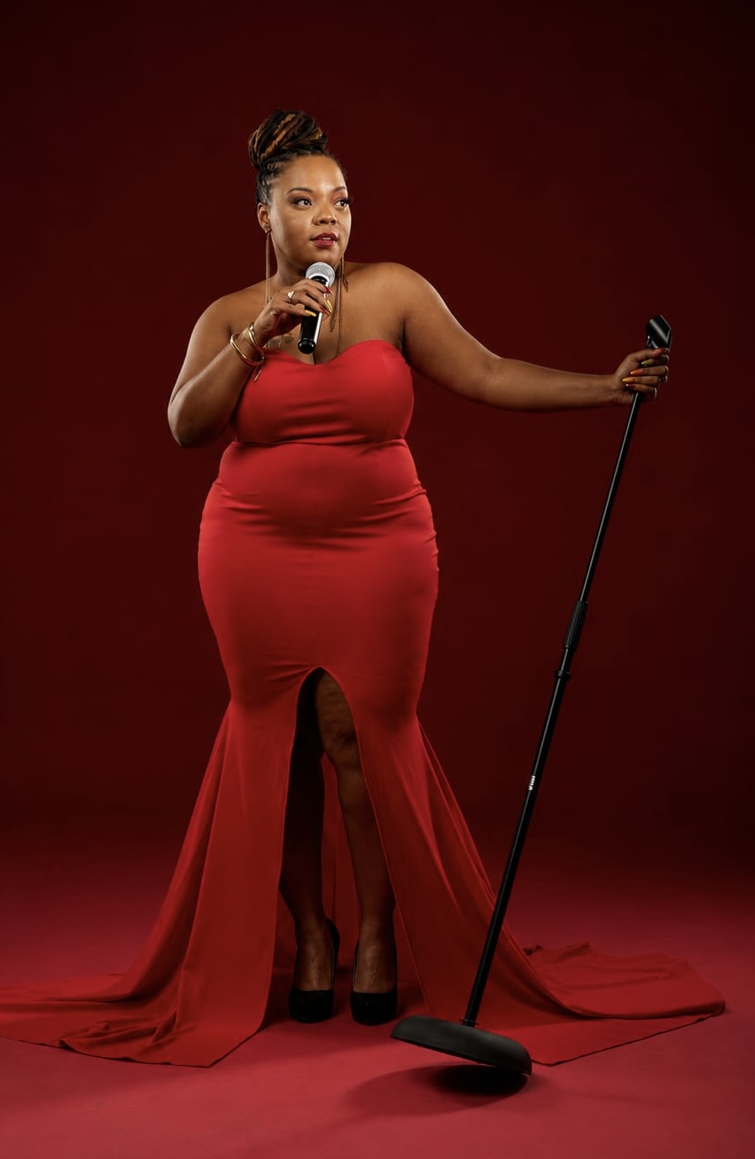 Erica Denise posing with a microphone in a red gown